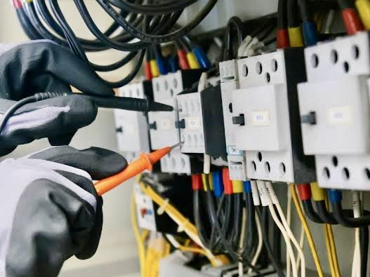 A bright, rustic kitchen featuring five glass globe pendant lights hanging from a wood-paneled ceiling. The space includes light wood cabinetry, a stainless steel refrigerator, and a large window overlooking a green backyard.